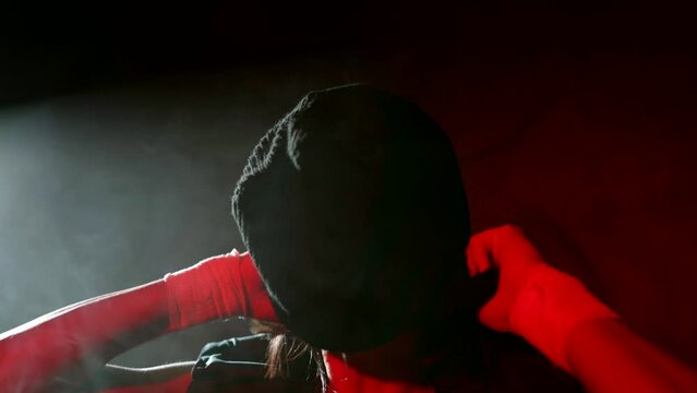 woman gangster or soldier putting black balaclava on her head in dark room or basement, closeup
