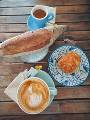 Overhead view of sourdough bread, chocolate croissant, espresso and cappuccino in a cozy cafe, autumn mood aesthetic