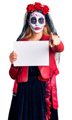 Woman wearing day of the dead costume holding blank empty banner pointing with finger to the camera and to you, confident gesture looking serious
