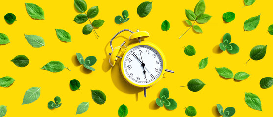 Yellow vintage alarm clock with green leaves - flat lay - obrazy, fototapety, plakaty