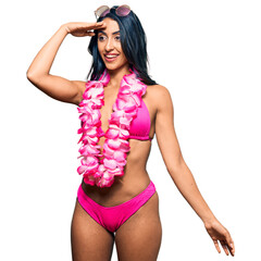 Beautiful hispanic woman wearing bikini and hawaiian lei very happy and smiling looking far away...