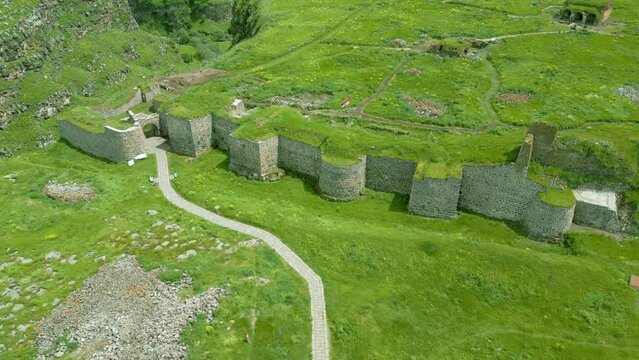 Aerial view of the medieval stone fortress, overgrown with grass, between canyons in summer in sunny weather. Armenian Lori fortress on the bank of the Dzoraget River in Lori Province. Drone footage.