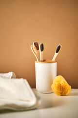Bamboo toothbrushes in a cup and a towel in a bathroom interior.