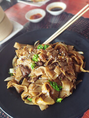 Vertical view of pad see ew or thai stir-fried noodles served in a black plate with chopsticks