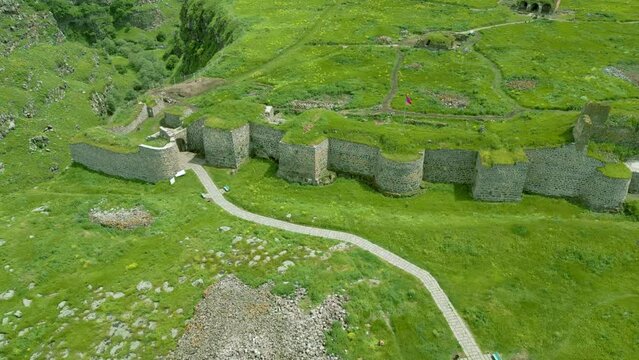 Aerial view of the medieval stone fortress, overgrown with grass, between canyons in summer in sunny weather. Armenian Lori fortress on the bank of the Dzoraget River in Lori Province. Drone footage.