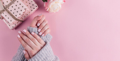 Stylish trendy female pink and silver manicure. Female hands on pink pastel background with rose...