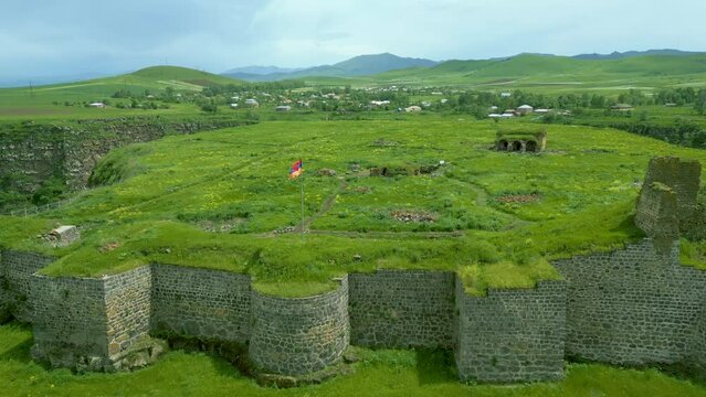Aerial view of the medieval stone fortress, overgrown with grass, between canyons in summer in sunny weather. Armenian Lori fortress on the bank of the Dzoraget River in Lori Province. Drone footage.
