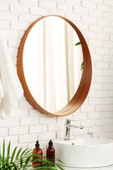 Bathroom interior with circle shaped mirror in wooden frame and white sink