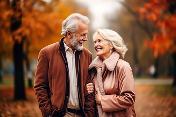 Fototapeta premium An elderly couple, a man and a woman, hugging in an autumn park. They look at each other with a loving gaze. Old people on a walk. Relationships in old age. Love and romance.