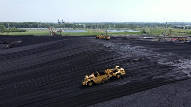 Industrial machine grading massive pile of coal for powerplant, aerial view