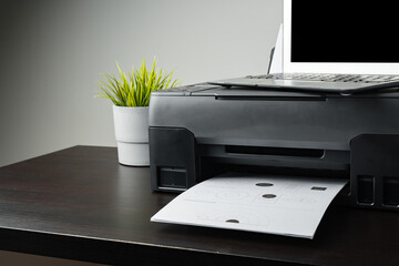 Modern printer with paper and laptop on table in office