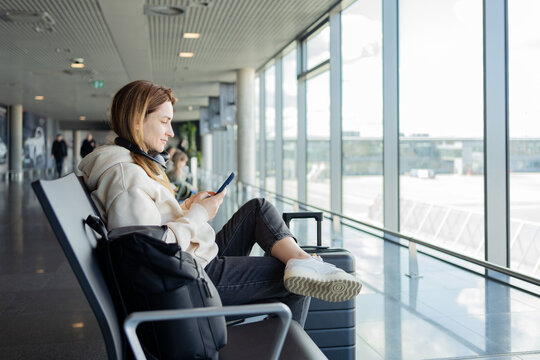 Woman use smartphone and earphones while waiting for her flight, student girl listening to music or podcast at the airport while waiting for a flight.