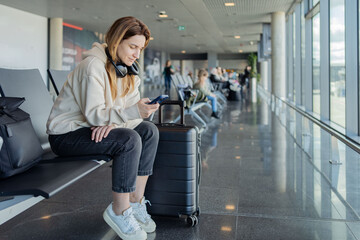 Woman use smartphone and earphones while waiting for her flight, student girl listening to music or...