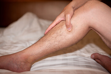 close up of man hand touching and massage calf on bed, leg cramp muscle pain