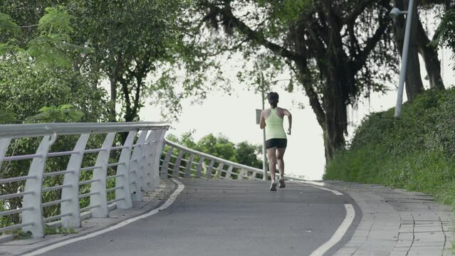 rear view of an asian young woman female jogger jogging running outdoors on road in park