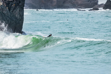 Fototapeta premium San Francisco, California, USA - October 23, 2021, A surfer rides a wave with cliffs in the background in San Francisco.