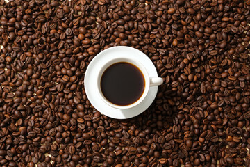 A cup of black coffee stands out against a background of coffee beans. Coffee has a unique aroma and is a popular drink that helps stay alert during work.