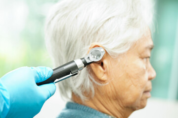 Otolaryngologist or ENT physician doctor examining senior patient ear with otoscope, hearing loss problem.