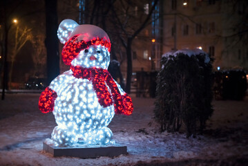 Glowing snowman in a red hat on the street in the evening