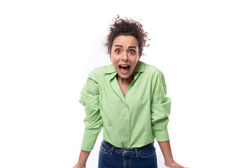 young brunette curly slender female model dressed in a light green shirt stands in confusion on a white background with copy space