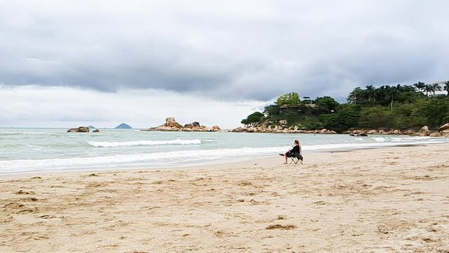 Lonely women sitting by seaside on chair. Lady in black.