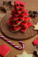 Christmas tree made of star shaped shortcrust cookies with red sugar glaze with cookie cutters candy canes and other cookies on wooden table. Christmas background