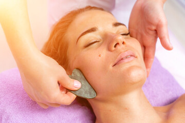 Obraz na płótnie Canvas Relaxing massage. European woman getting quartz guache face massage in spa salon, side view