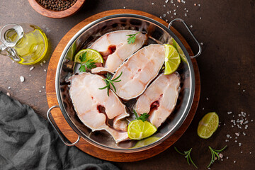 Raw catfish steaks with herbs, lime and spices in a baking dish on a dark background top view