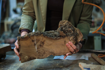 Hands hold a slab of burl wood with intricate grain, highlighting the natural artistry that woodworkers cherish and transform into fine objects.