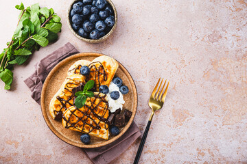 Homemade waffles with blueberries, chocolate sauce and cream cheese in a plate and a beige background top view copy space for text