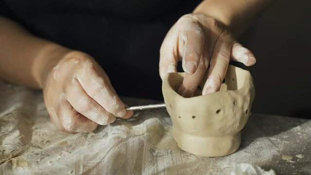 A woman makes holes using a tool in a clay craft - a candlestick. Close-up. Hobbies and creativity.