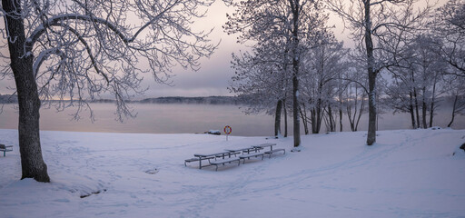 Fototapeta na wymiar Smoke, fog, over the lake Mälaren at a beach, frost on trees and snow in the Stockholm district Bromma