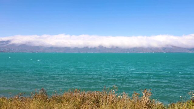 Clouds shroud mountain peaks and descend to Lake Sevan on a sunny summer day, time lapse