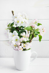 A beautiful sprig of an apple tree with white flowers in a cap against a white wooden background. Blossoming branch in a glass with water. Spring still life. Concept of spring or mom day