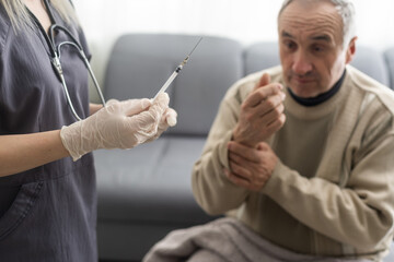 Doctor giving vaccination shot to elderly patient by syringe or injunction at home. concept of home...