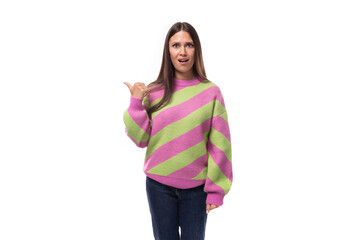 young caucasian woman with black hair dressed in a pink striped sweater points with her hand on a white background with space for advertising