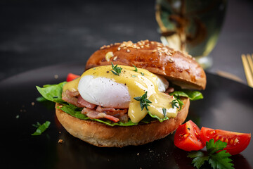 Breakfast. Sandwich with ham, poached egg, onion and arugula in a plate on a dark background