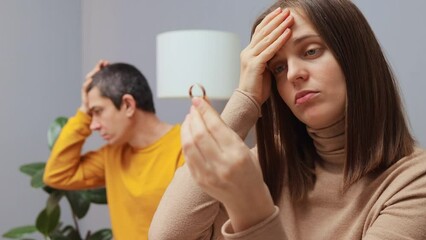 Attractive serious woman removing wedding ring from finger despaired husband sitting on background with negative sad feelings couple having problems in relationship thinking about divorce