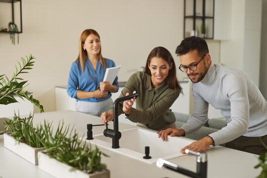 Female shop assistant helping young couple choose new kitchen faucet