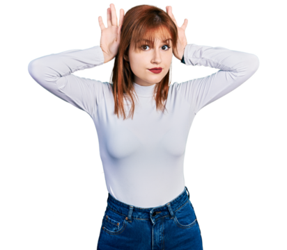 Redhead young woman wearing casual turtleneck sweater doing bunny ears gesture with hands palms looking cynical and skeptical. easter rabbit concept.