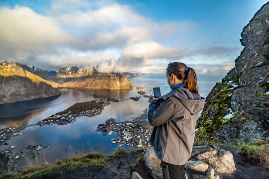 young woman taking a Picture with phone from the height of Reinebringen on fisherman reine village on lofoten islands in norway