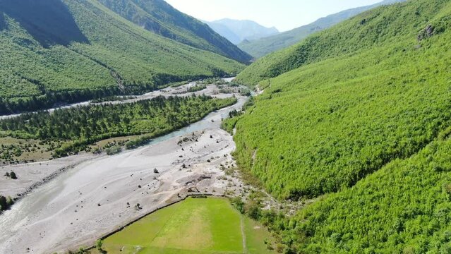 Drone view in Albania in the alps flying over a crystal river with rocky ground with green forest on the sides in Theth