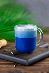 Blue matcha latte tea drink from clitoria flowers on a wooden board with palm branch. Healthy drink, lactose, gluten and sugar free.