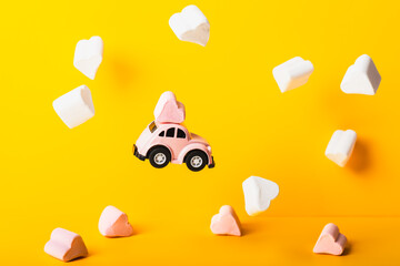 A small model of a pink car with marshmallows in the shape of a heart flies in marshmallow clouds...