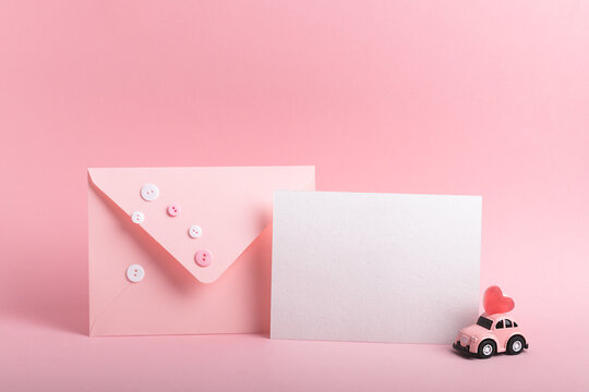 Pink envelope, blank card and small pink car model with heart shaped jelly beans on a pink background.