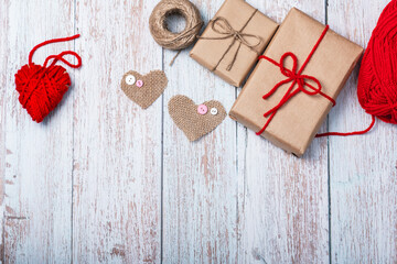 Two gift boxes, hearts made of burlap and red threads, a ball of twine on a wooden background. DIY gifts. Copy space.