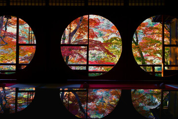 Beautiful autumn leaves viewed through the round window of a traditional Japanese house and...