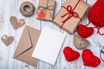Craft envelope, blank form, heart shapes made of burlap, red thread and twine and two craft gift boxes on a wooden background. DIY gifts for Valentine's Day.