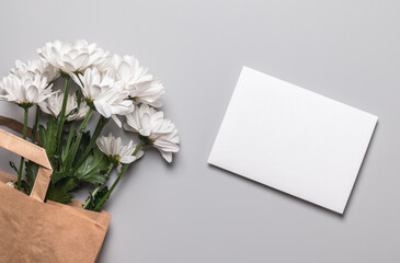 Craft envelope, blank form and bouquet of white chrysanthemums in a gift bag on a gray background with copy space. Postcard, mockup.