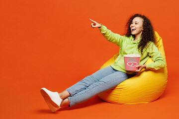 Full body shocked young woman she wear green hoody casual clothes sit in bag chair eat popcorn...